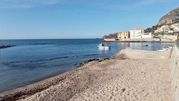 A beach with a rocky shoreline, a boat, and buildings in the background.