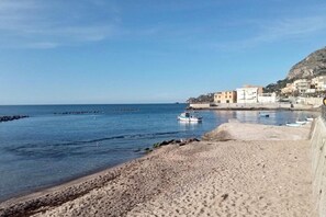A beach with a rocky shoreline, a boat, and buildings in the background. - Belvilla by OYO CasaAmare (Bagheria)
