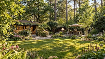 Een verzorgde tuin met een houten huisje, een terras met tuinmeubilair, en diverse planten en bloemen.