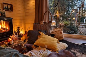 Una sala de estar acogedora con chimenea, un sofá cómodo, una cesta y vistas al exterior.