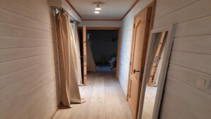 A narrow hallway with wooden walls and a wooden floor. There are doors on both sides, one of which is open.