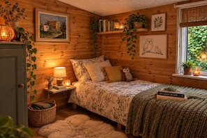 Un dormitorio acogedor con cama, mesita de noche, lámpara y una ventana con plantas.