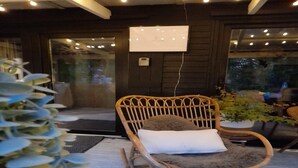 A wicker rocking chair with a white cushion, a potted plant, and a wall-mounted light fixture.