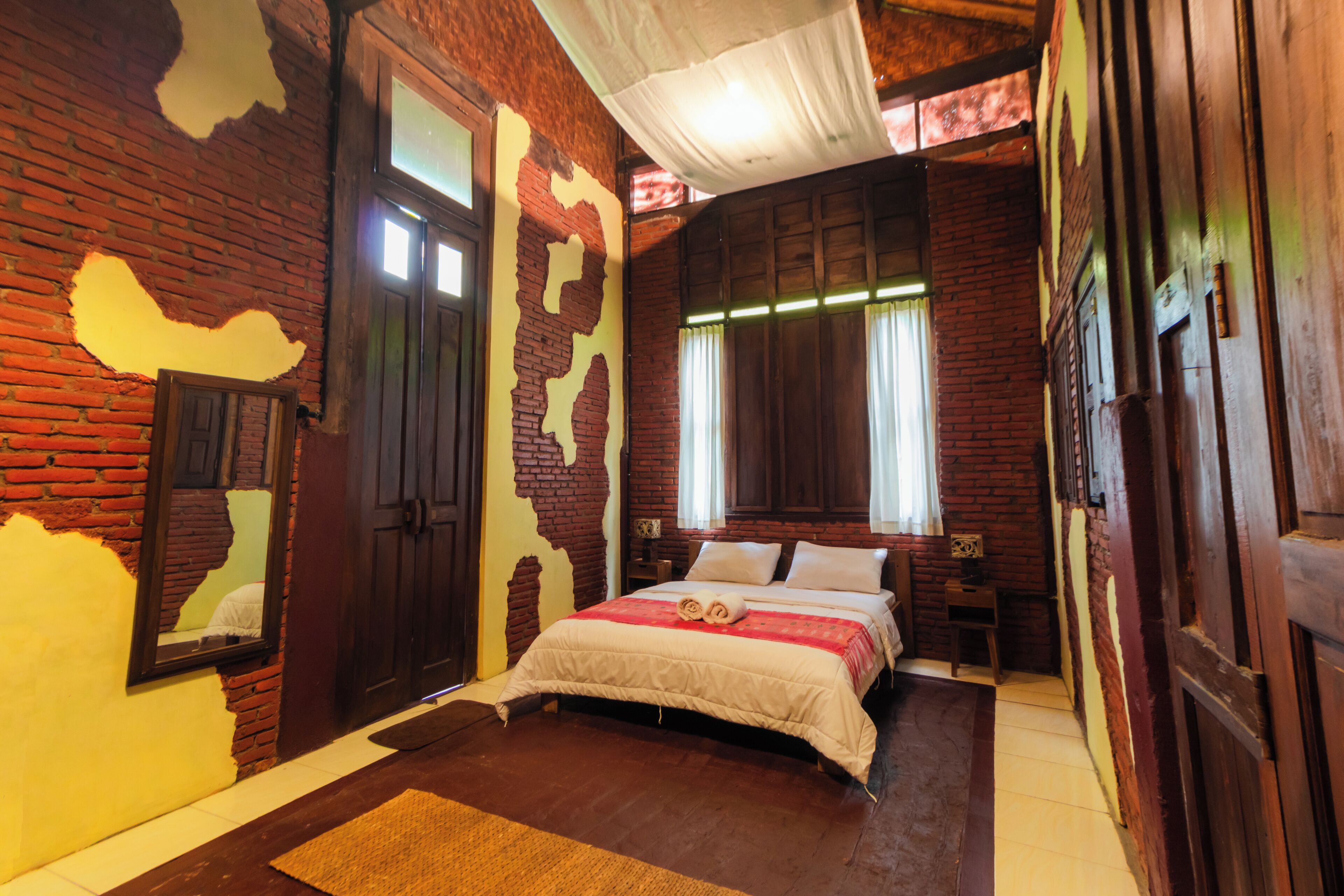 A room with a brick wall, wooden door, and a bed with a white bedspread and pillows.