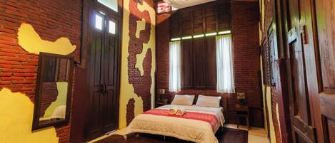 Une pièce avec un mur en briques, une porte en bois et un lit recouvert d’une couverture blanche et agrémenté d’oreillers.