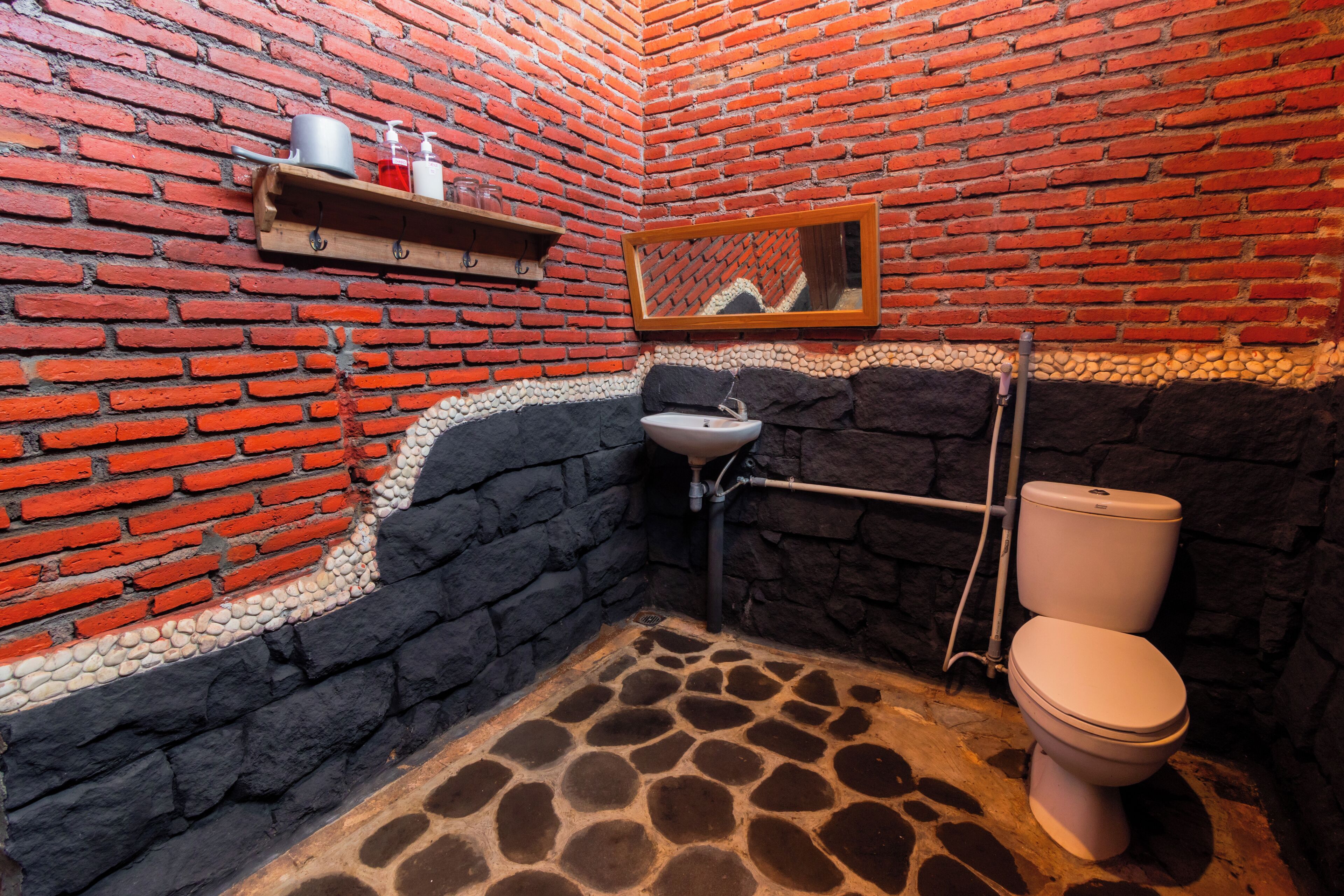 Une salle de bain avec un mur en briques, un sol en pierre, un lavabo et des toilettes.