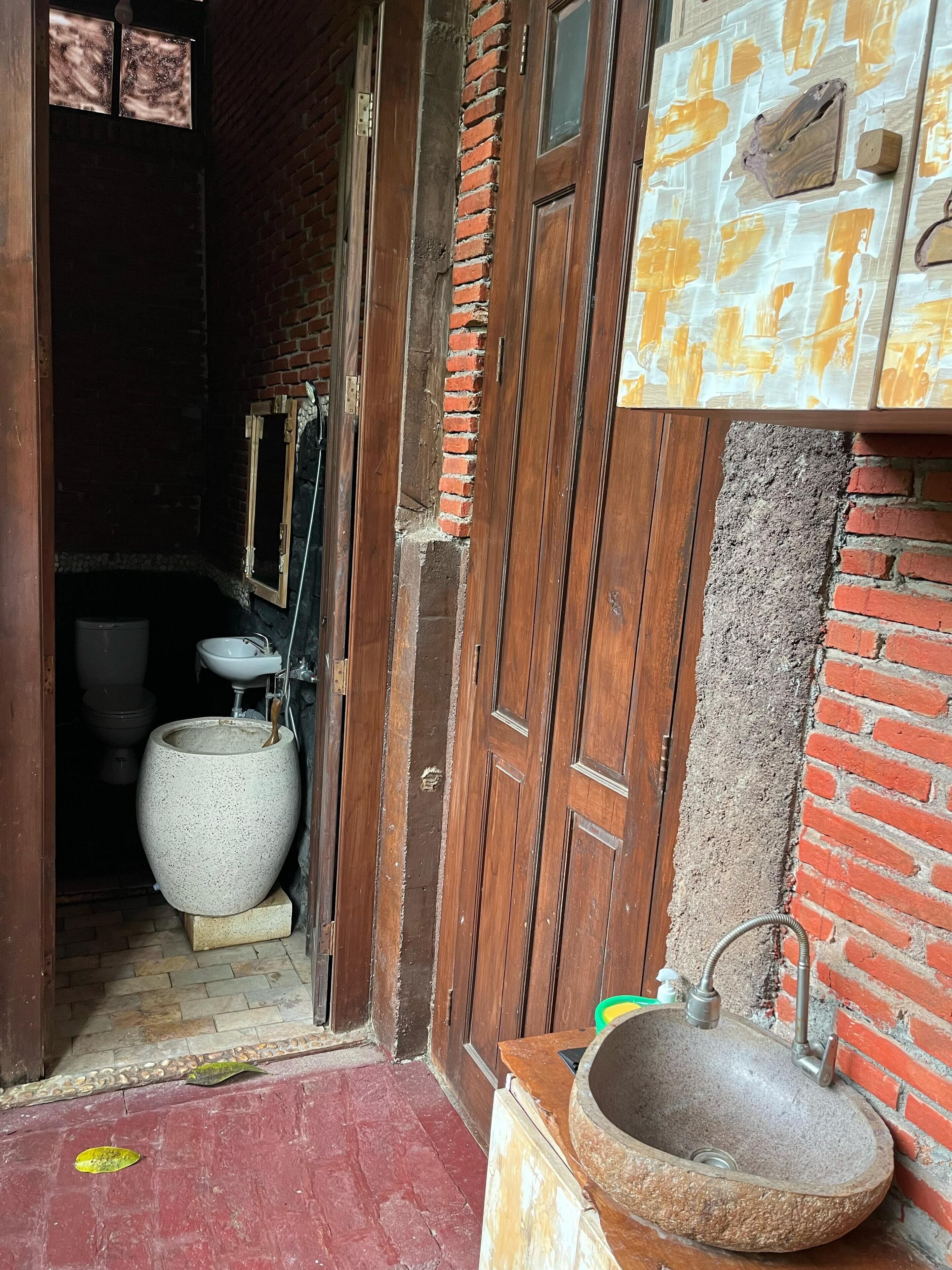 A rustic bathroom with a large ceramic sink, a wooden door, and a brick wall.