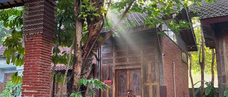 A traditional wooden building with a tiled roof, surrounded by lush greenery and a stone pathway.