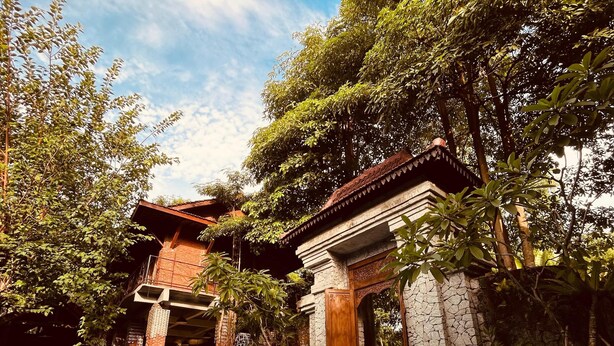 A clear blue pool with a stone structure and a wooden building in the background. - Djawata resort & gallery  (Bangunjiwo)