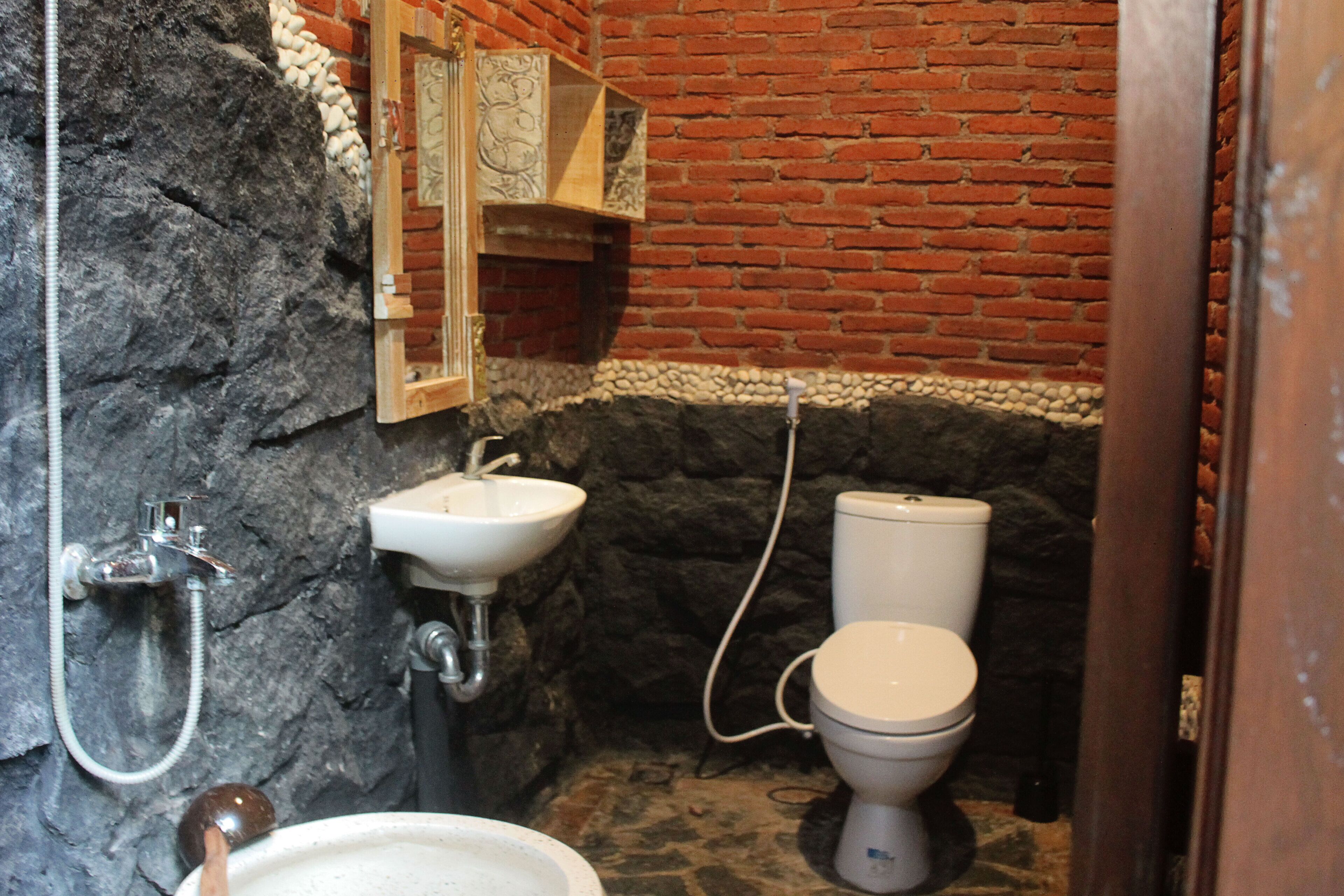 A bathroom with a stone wall, a white sink, a toilet, and a wooden cabinet.