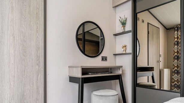 Et moderne badeværelse med et rundt spejl, et lille toiletbord, toilet og bruseområde.