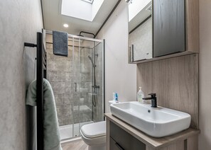 Un baño moderno con cabina de ducha de vidrio, inodoro, lavabo con espejo y toallero.