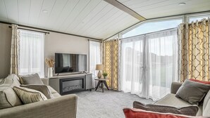 En moderne stue med et fladskærms-tv, sofaer, en pejs og store vinduer med gardiner.