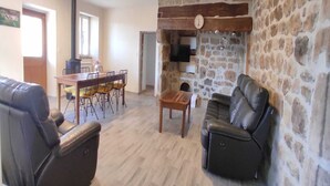 A living room with a stone wall, a fireplace, a dining area with a table and chairs, and leather sofas.