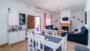 A modern living room with a fireplace, a dining area with white furniture, and a kitchen with white cabinets and a microwave. - Holiday Home "Casa Rural Rafael" with Private Pool, Private Terraces & Wi-Fi (Lantejuela)