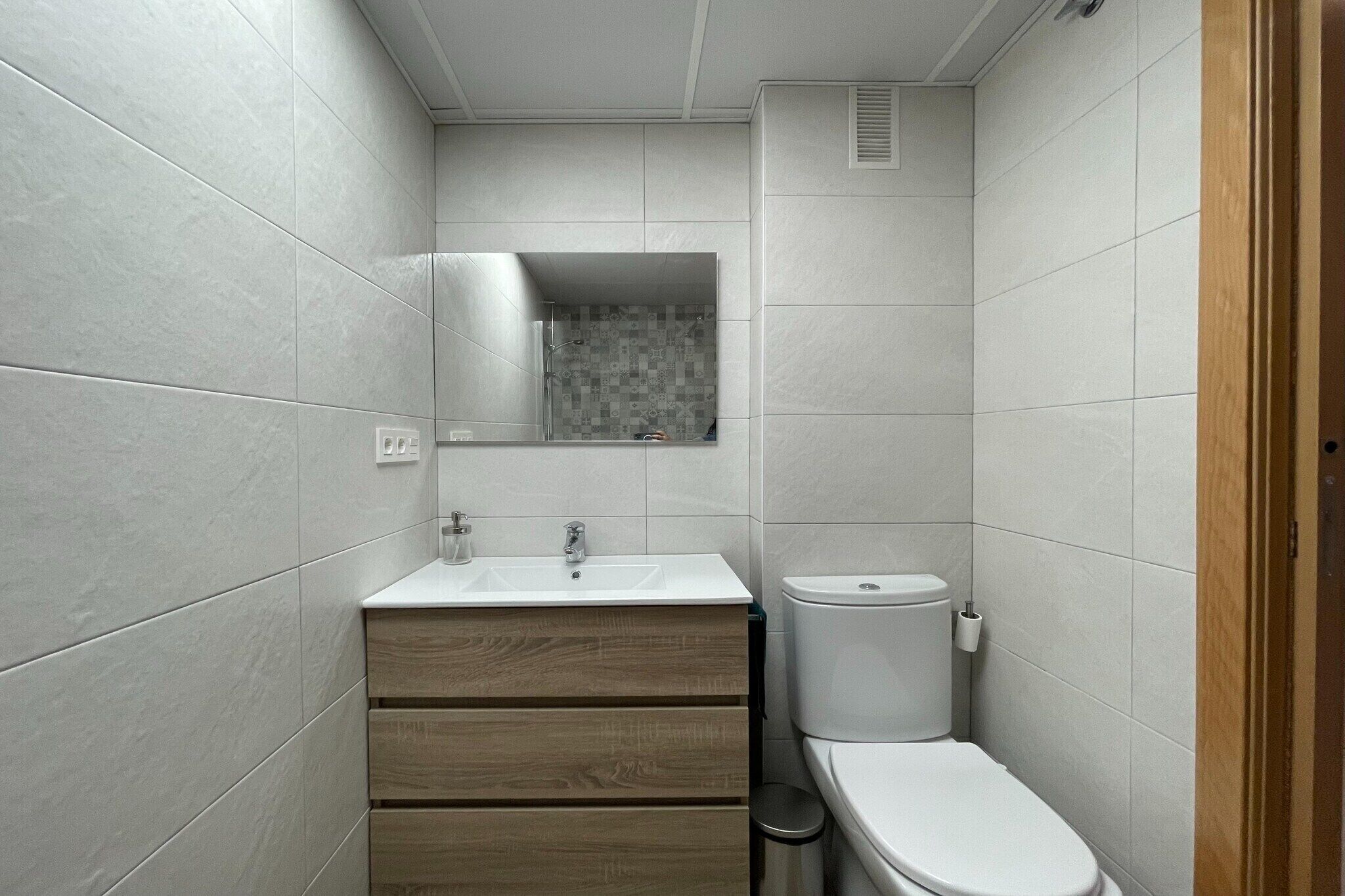 Un baño pequeño y moderno con lavamanos blanco, tocador de madera y un inodoro.