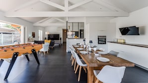 A modern kitchen with a dining area, a foosball table, and a TV mounted on the wall. - Villa Sirelis with Pool and Spa (Gujan-Mestras)