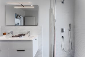 Een moderne badkamer met een wit wastafelmeubilair, een grote spiegel, een douche met een handdouche en een gestructureerde wand.