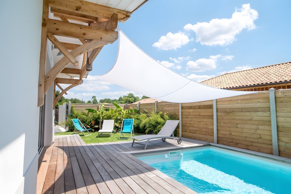 Une terrasse en bois avec une piscine, deux chaises longues et un auvent blanc.