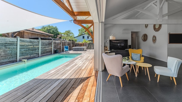 A modern outdoor patio with a pool, wooden deck, and seating area. - Villa Sirelis with Pool and Spa (Gujan-Mestras)