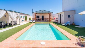 Una piscina con bordo in mattoni, una veranda coperta e un edificio con tetto verde.