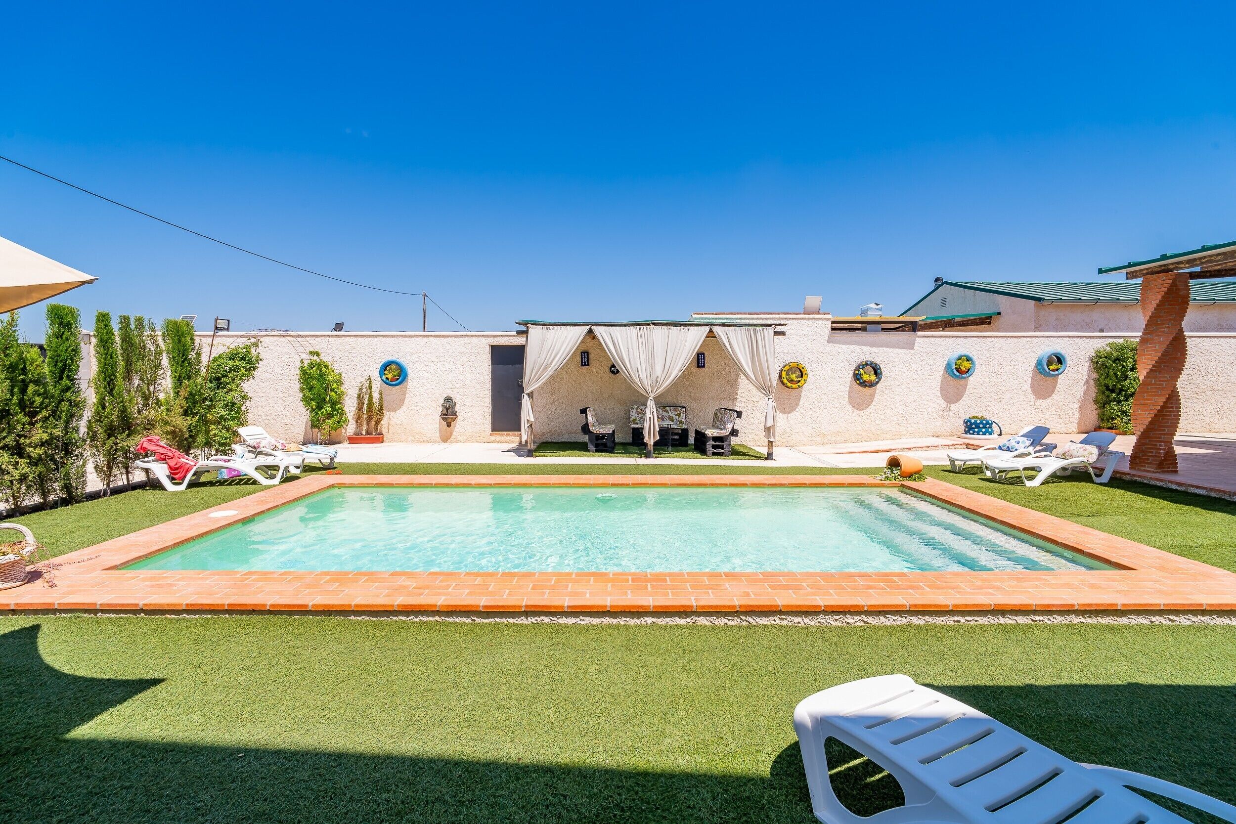 A swimming pool with a tiled border, surrounded by artificial grass and white lounge chairs.