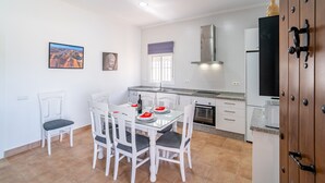 Una cucina moderna con mobili bianchi, un tavolo da pranzo con sedie, una finestra con persiane e una statua di Buddha sulla parete.