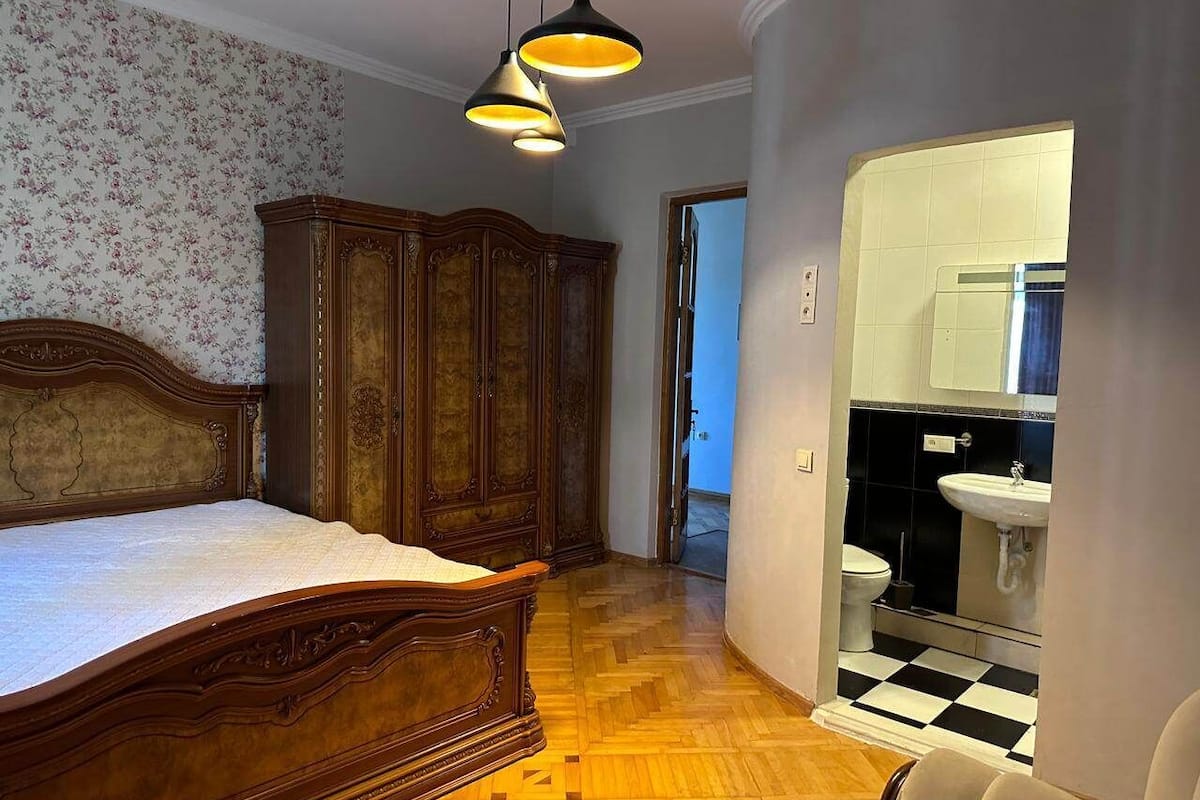 A bedroom with a wooden bed, a wardrobe, and a bathroom with a checkered floor.