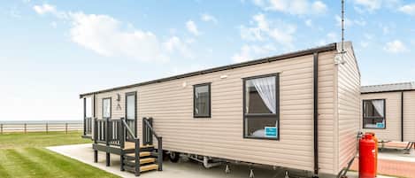 A mobile home with a porch, a window with a curtain, a sign, and a red fire extinguisher.