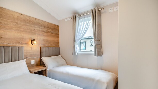 Un dormitorio con dos camas, cabeceros de madera, una mesita de noche con lámpara y una ventana con cortinas.
