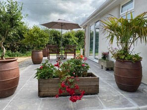An outdoor patio with potted plants, a wooden bench, and an umbrella. - Toppesfield House (Bude)