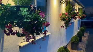 Un edificio con fachada blanca, ventanas con macetas de flores y un camino de grava.