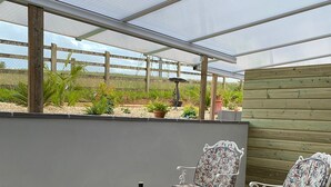An outdoor patio with wicker furniture, a table with a bottle and glasses, and a view of the beach through a wooden fence. - Toppesfield House (Bude)