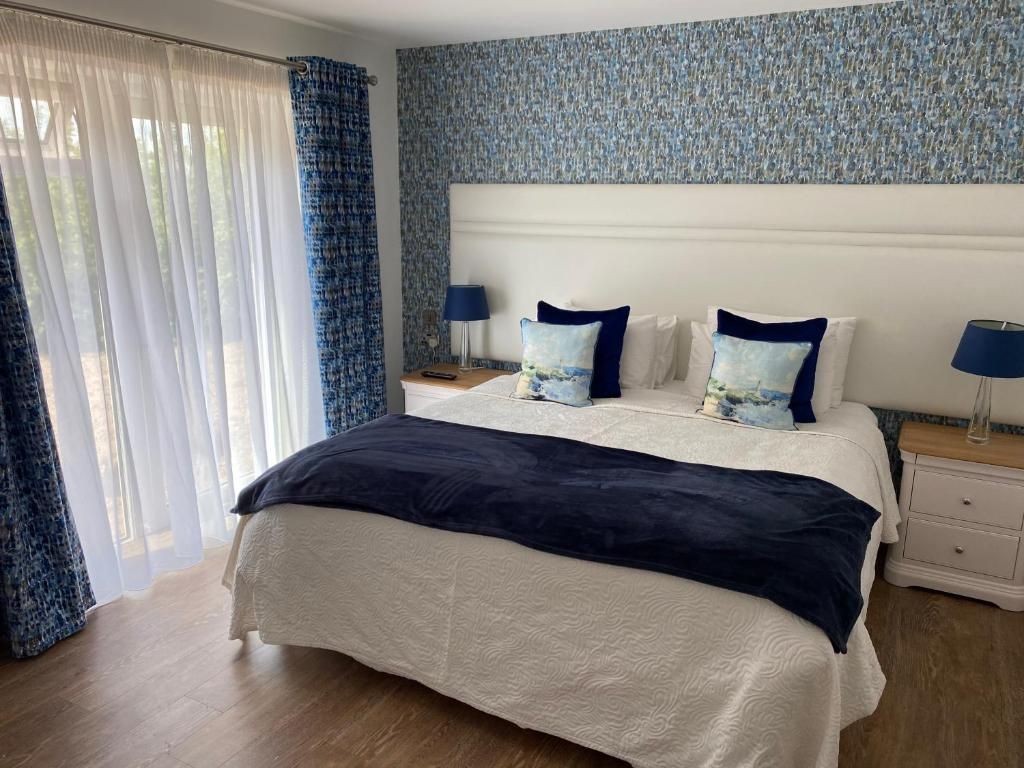A hotel room with a bed, two bedside tables, a nightstand, and a window with curtains.