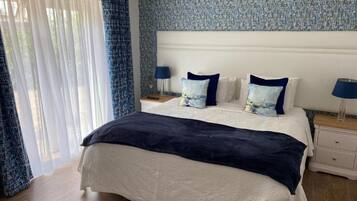 A hotel room with a bed, two bedside tables, a nightstand, and a window with curtains.