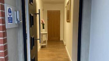 A hallway with a wooden floor, a door at the end, and a wall-mounted sign.