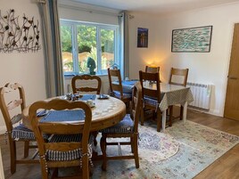 Un comedor con una mesa redonda, sillas de madera, un tapete estampado y una ventana con cortinas.