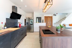 A modern kitchen with dark cabinetry, a wooden island, a built-in oven, and a stainless steel refrigerator. - Villa 'Mas Mayflower' with Mountain View, Wi-Fi, and Air Conditioning (Cabrières-d'Avignon)