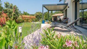 Eine moderne Außenpatio mit überdachter Sitzecke, ein Garten mit verschiedenen Pflanzen und ein Holzzaun im Hintergrund.