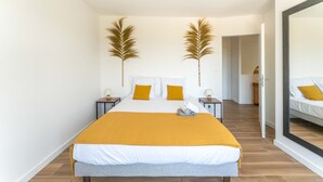 Ein Schlafzimmer mit einem Bett, zwei Nachttischen, einem Spiegel und einer Tür zu einem weiteren Raum.