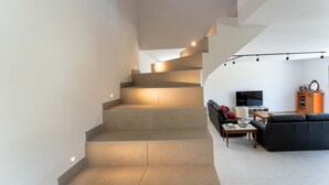 Ein modernes Interieur mit einer Treppe, einem Wohnbereich mit Sofa, Fernseher und Bücherregal.