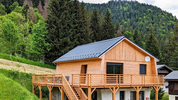 Een houten chalet met een balkon, een trap en uitzicht op een beboste helling.