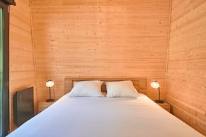 Ein Zimmer in einer Holzhütte mit einem Bett, zwei Nachttischlampen und einem Fenster.