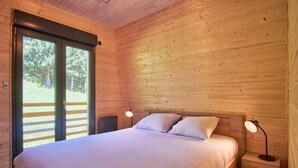 Een houten slaapkamer met een logies, twee bedlampen en een schuifglazen deur naar een terras.