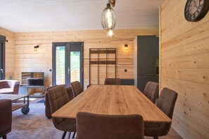 Ein Zimmer mit Holzwandverkleidung, einem großen Holztisch, mehreren Stühlen, einem Fernseher und einer Wanduhr.