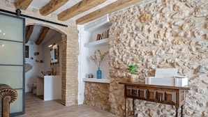Un interior rústico con paredes de piedra vista, una mesa de madera y una puerta que conduce a otra habitación.