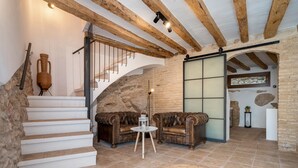 Una escalera con peldaños blancos que conduce a una plataforma, un sofá de cuero marrón, una mesita redonda con un farol y un ventanal con paneles de vidrio esmerilado.