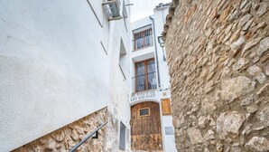 Una calle estrecha con un edificio de piedra, una puerta de madera y un letrero que dice 'El Raco de Les Escales'.
