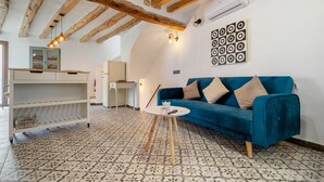 Una habitación con un sofá azul, un armario blanco, suelo estampado y vigas de madera a la vista.