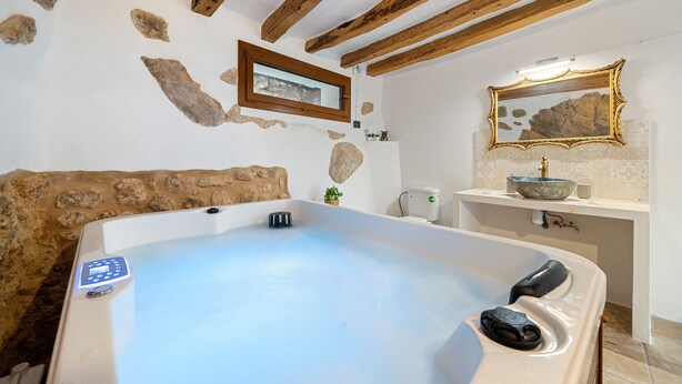 Un baño con bañera, techo de madera, pared de piedra, ventana y espejo.